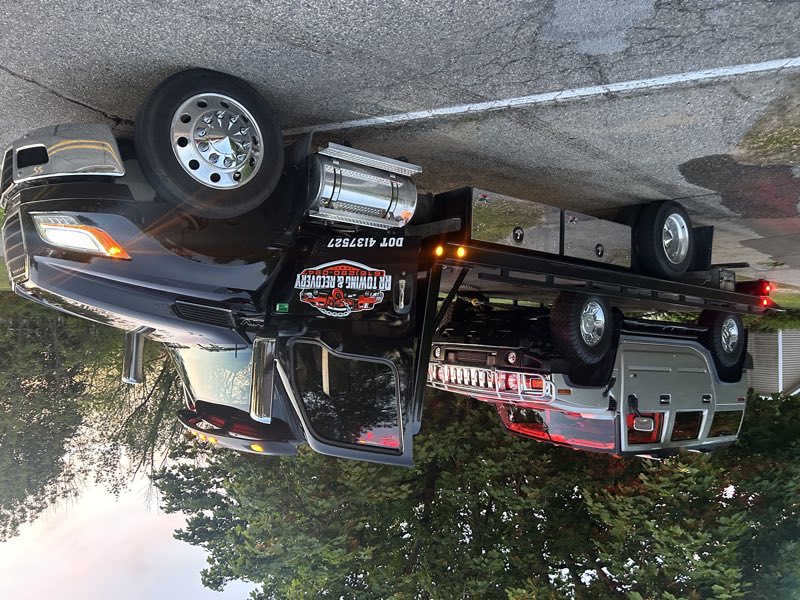 Black RR Towing & Recovery flatbed carrying a silver Hummer H2 at dusk
